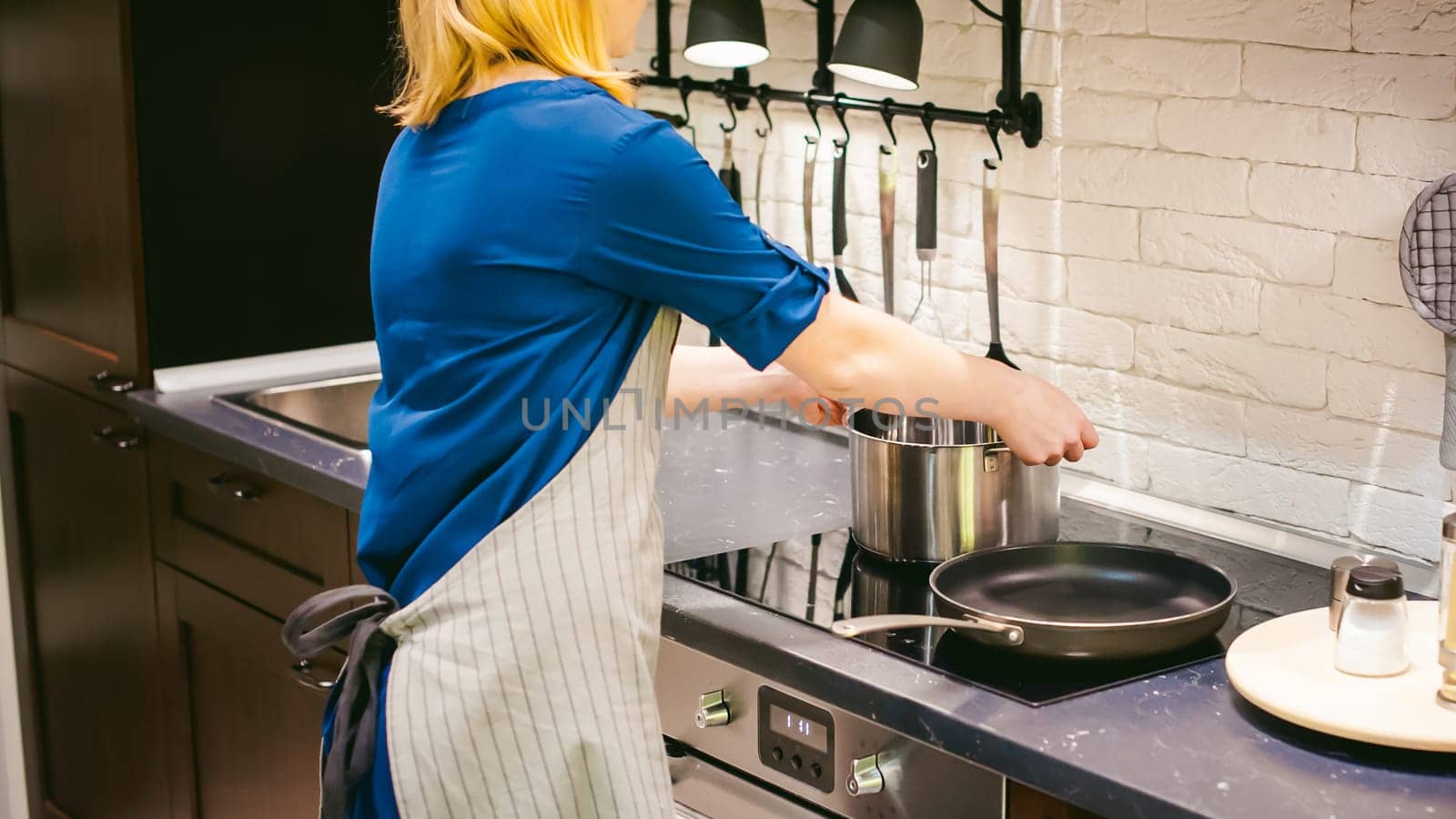 blonde woman with a pot in the kitchen. housewife in apron has been cooking in the kitchen, put pots and pans on the hob