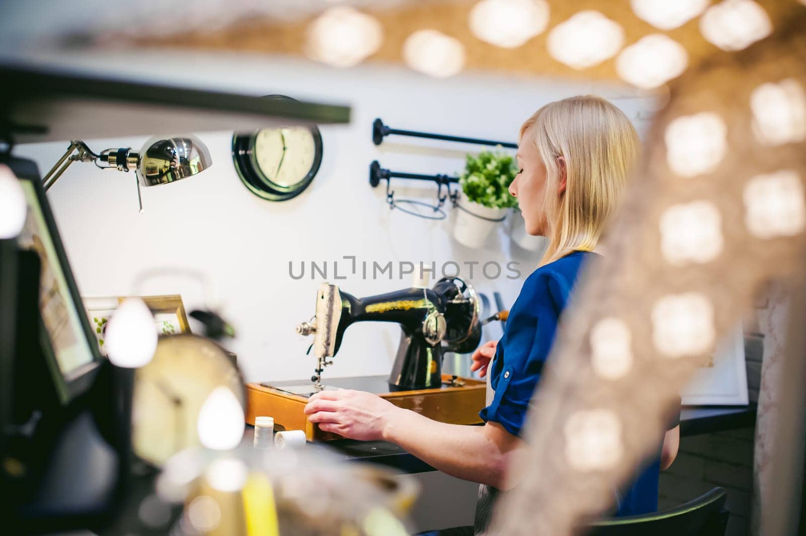 seamstress work on the sewing machine. young blonde woman working on a mechanical sewing machine at home sitting at your desk, be prepared to sew