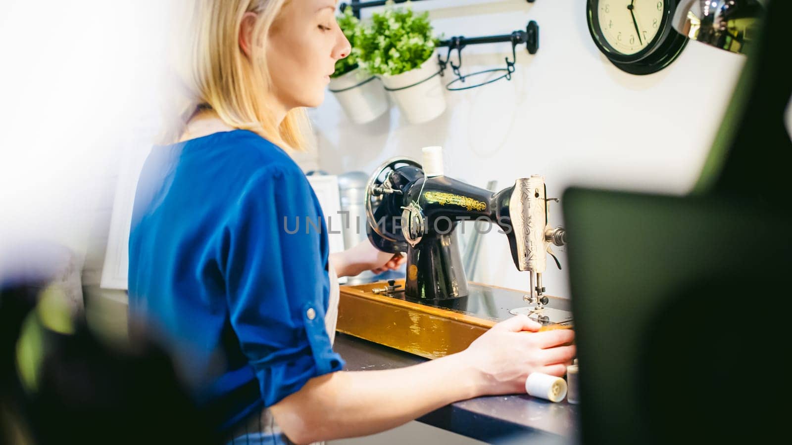 seamstress work on the sewing machine. young blonde woman working on a mechanical sewing machine at home sitting at your desk, be prepared to sew