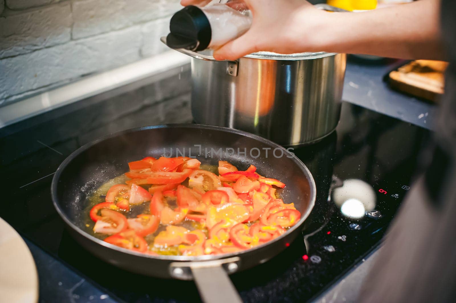 woman housewife prepares fried eggs with ham and vegetables in his kitchen. adds salt peppers and tomatoes in a pan