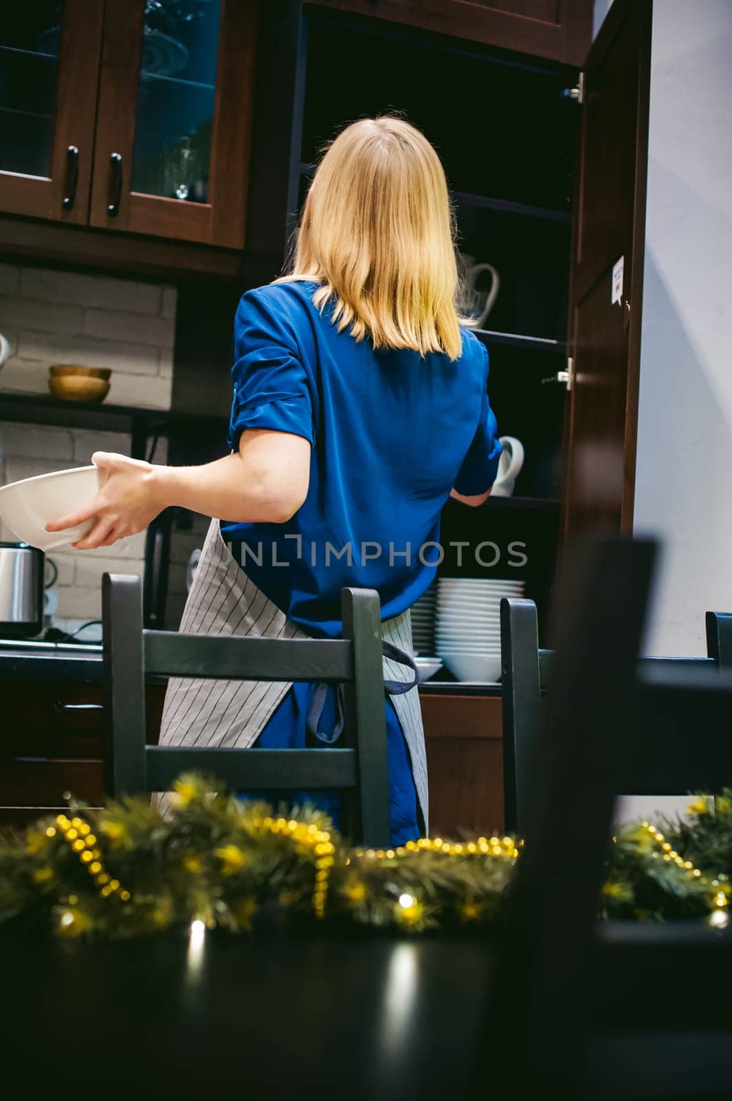 woman housewife in the kitchen. girl pulls out from the shelf cupboard dishes for table service. against the background of the Christmas tree