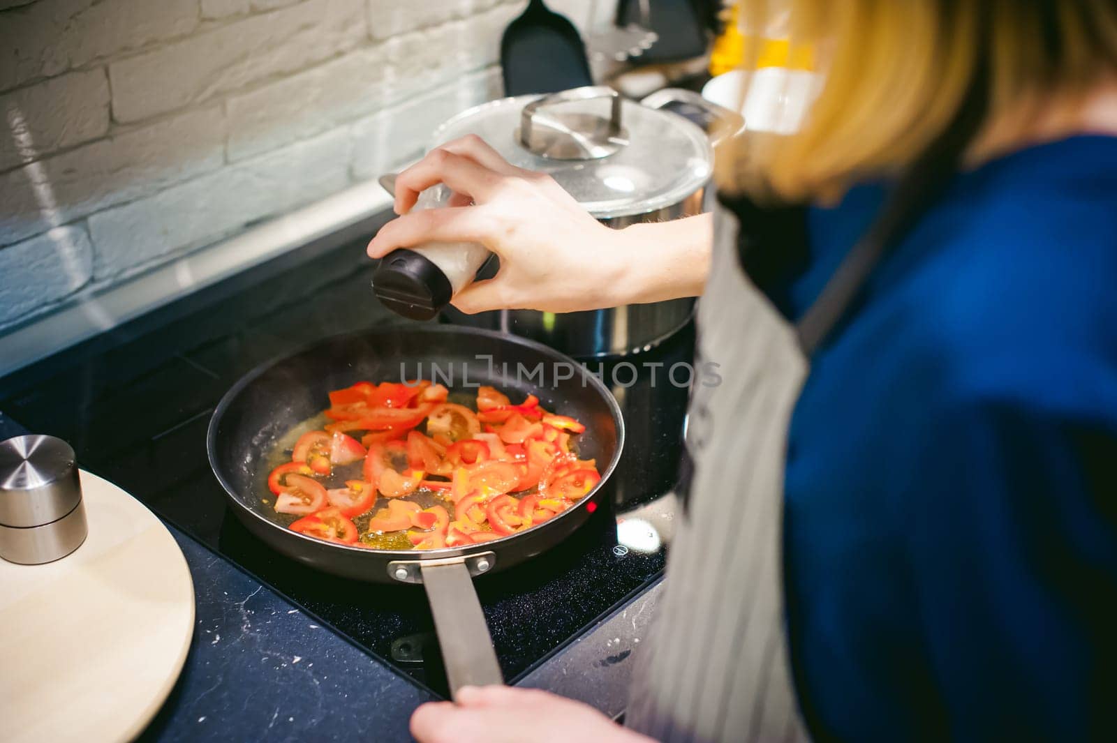 woman housewife prepares fried eggs with ham and vegetables in his kitchen. adds salt peppers and tomatoes in a pan