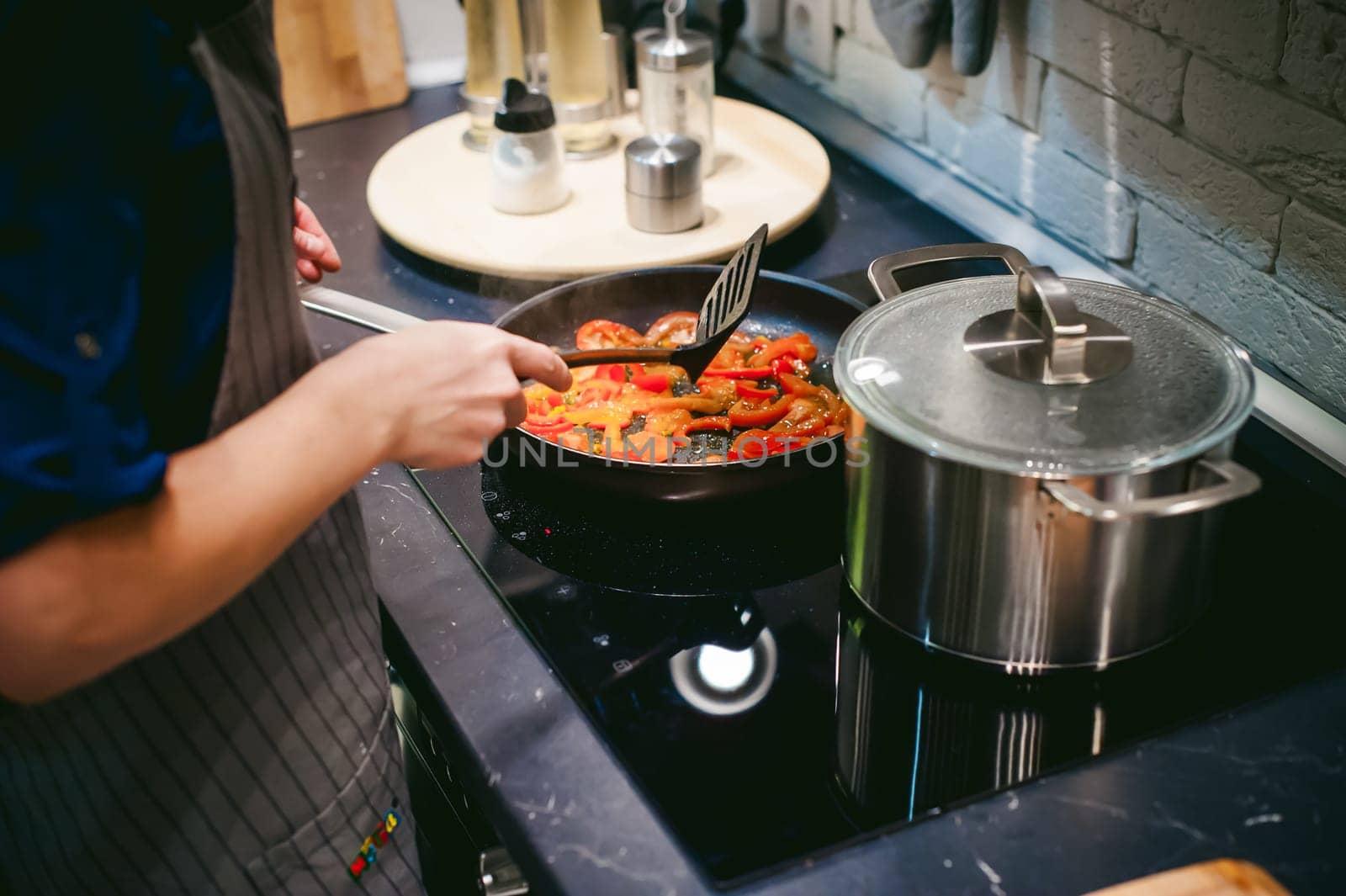 woman housewife prepares fried eggs with ham and vegetables in his kitchen. stir peppers and tomatoes in a pan