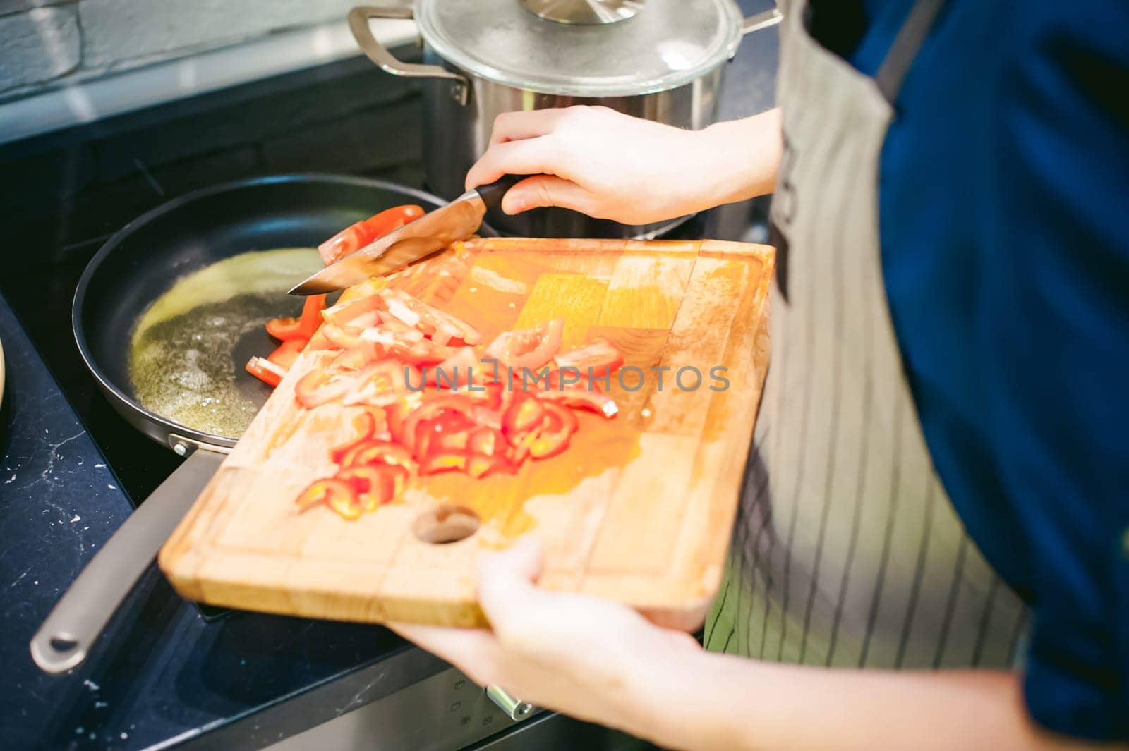 woman housewife prepares fried eggs with ham and vegetables in his kitchen. cut peppers and tomatoes, and puts them in a frying pan