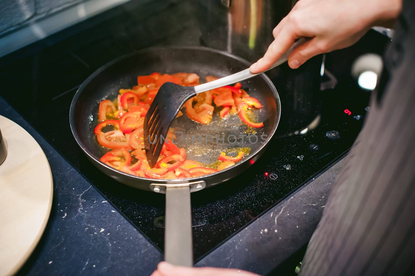 woman housewife prepares fried eggs with ham and vegetables in his kitchen. stir peppers and tomatoes in a pan