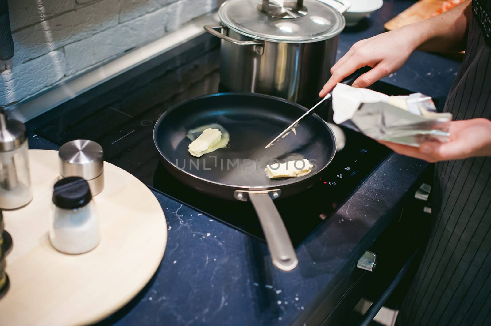 woman housewife prepares fried eggs with ham and vegetables in his kitchen. spreads the butter in the pan