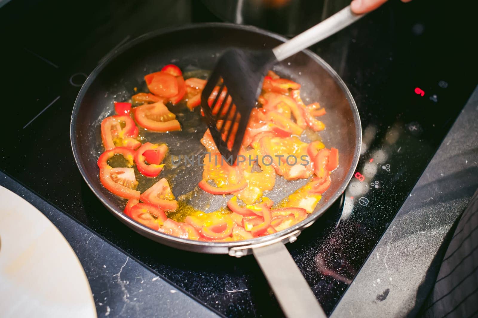 woman housewife prepares fried eggs with ham and vegetables in his kitchen. stir peppers and tomatoes in a pan