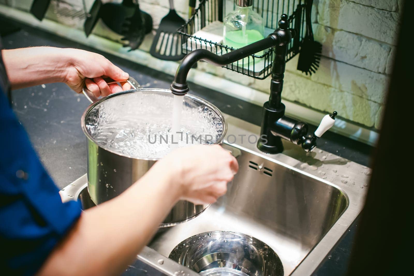 woman housewife in the kitchen. girl collects water from the tap in the pan