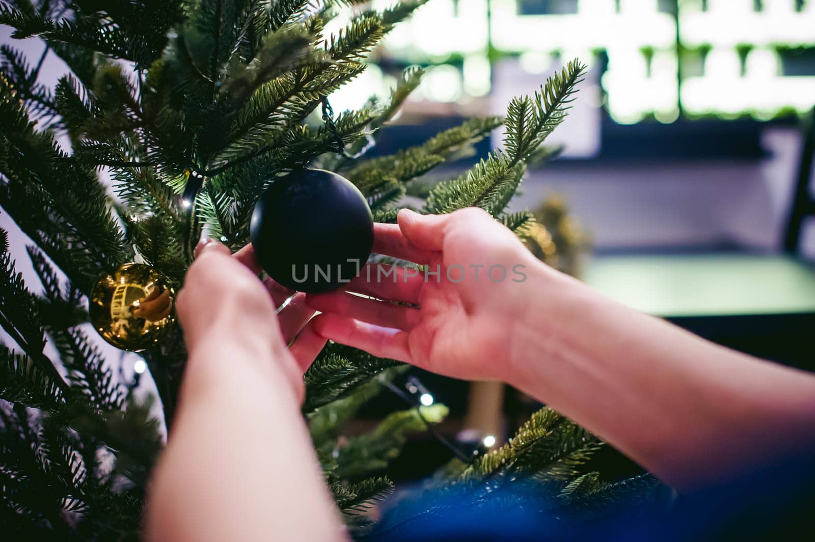 Female hands decorating a Christmas tree. girl decorates a festive Christmas tree, balls and toys Ornamental, at home in the cozy atmosphere of holiday