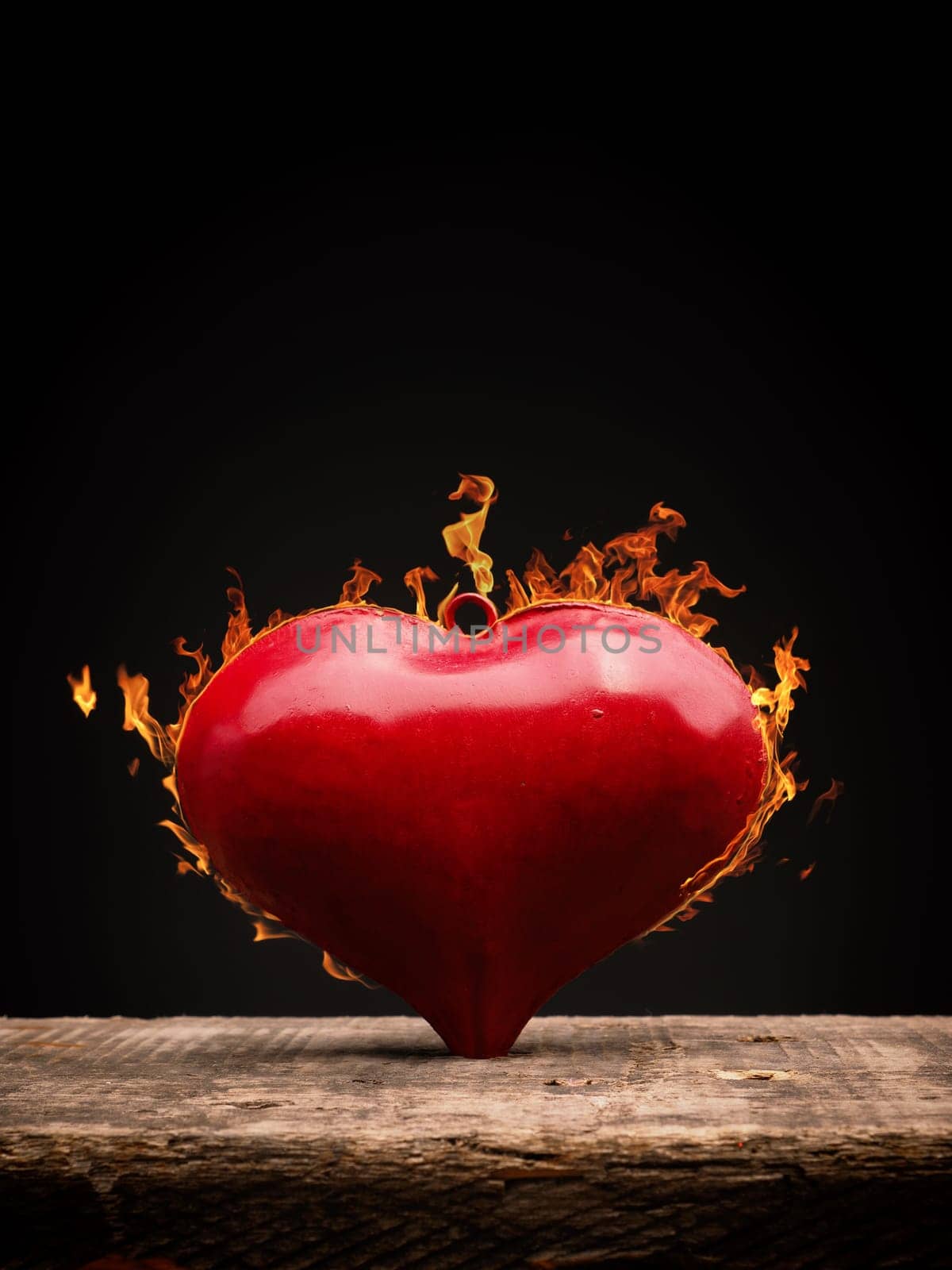 Burning heart, red metal heart shape with flames on a wooden table, love or Valentines Day concept background