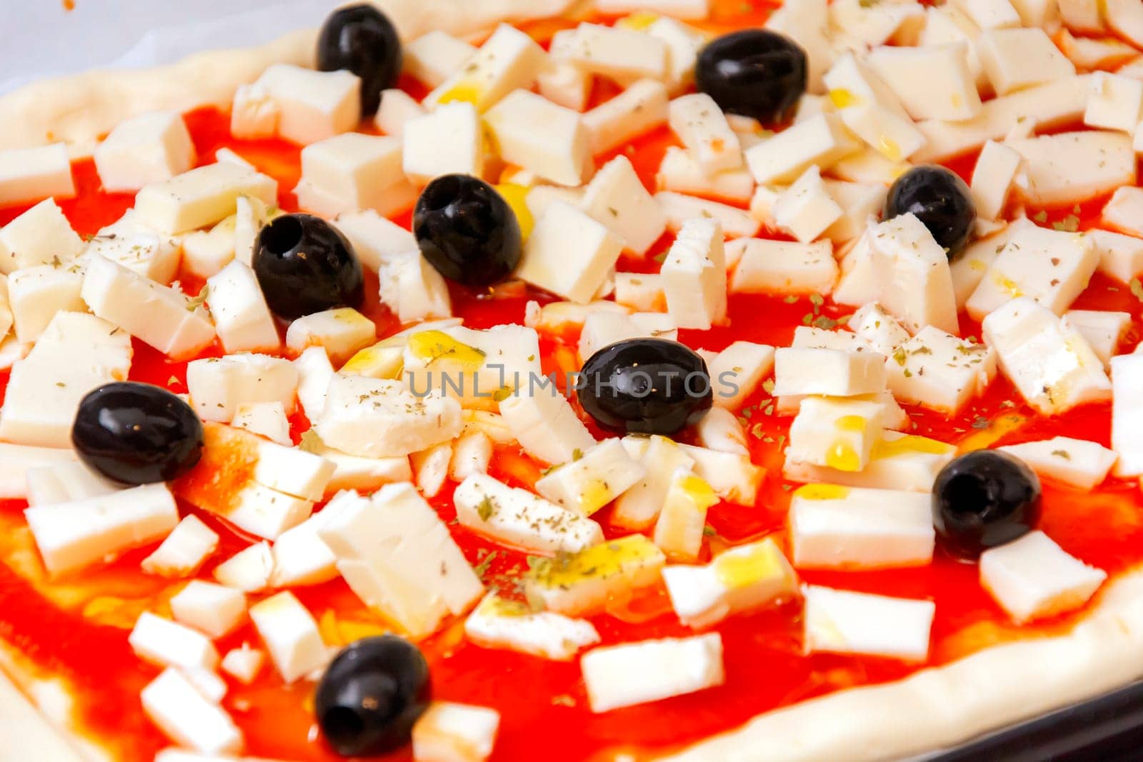 Raw pizza decorated mozzarella, black olives and tomato sauce ready to be baked