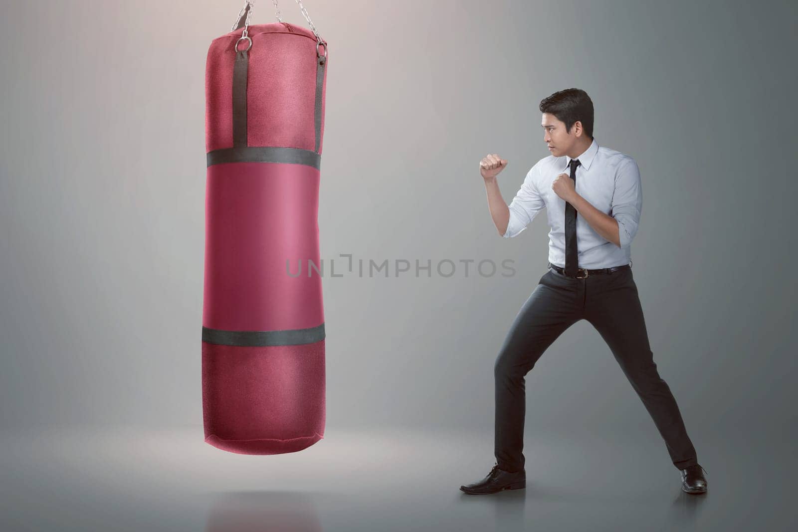 Young asian businessman punching boxing bag over gray background