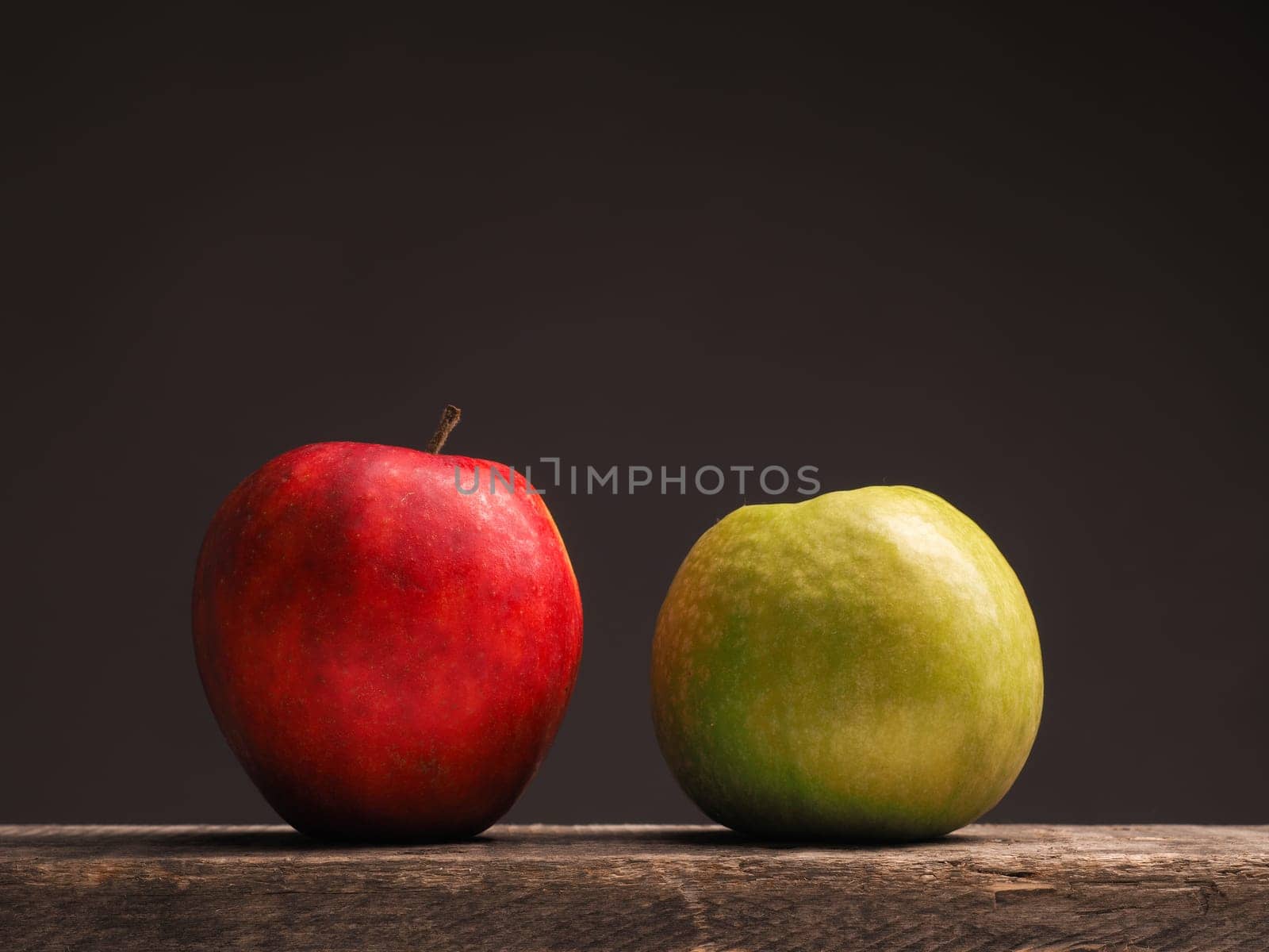 One green apple and one red apple on a rustic wooden table with place for text