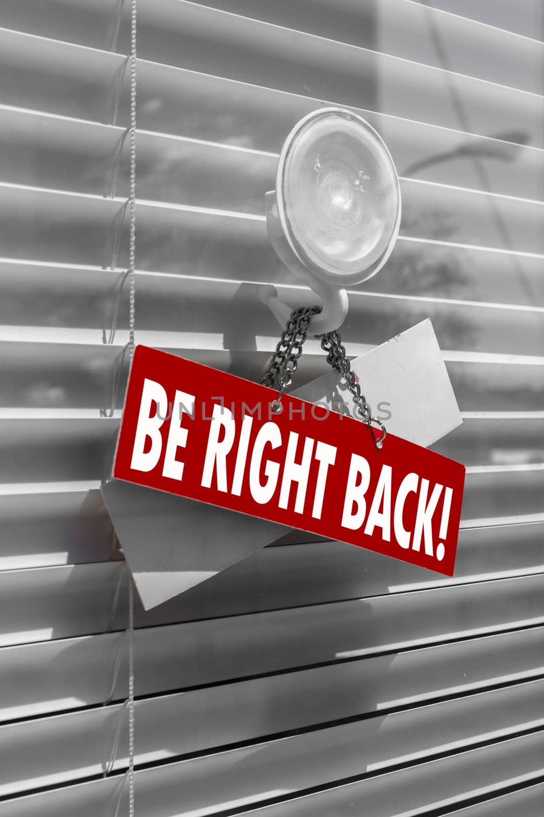 A sign saying "be right back"" on a glass door with a white, closed venetian blind. It can be used for business concepts or backgrounds."