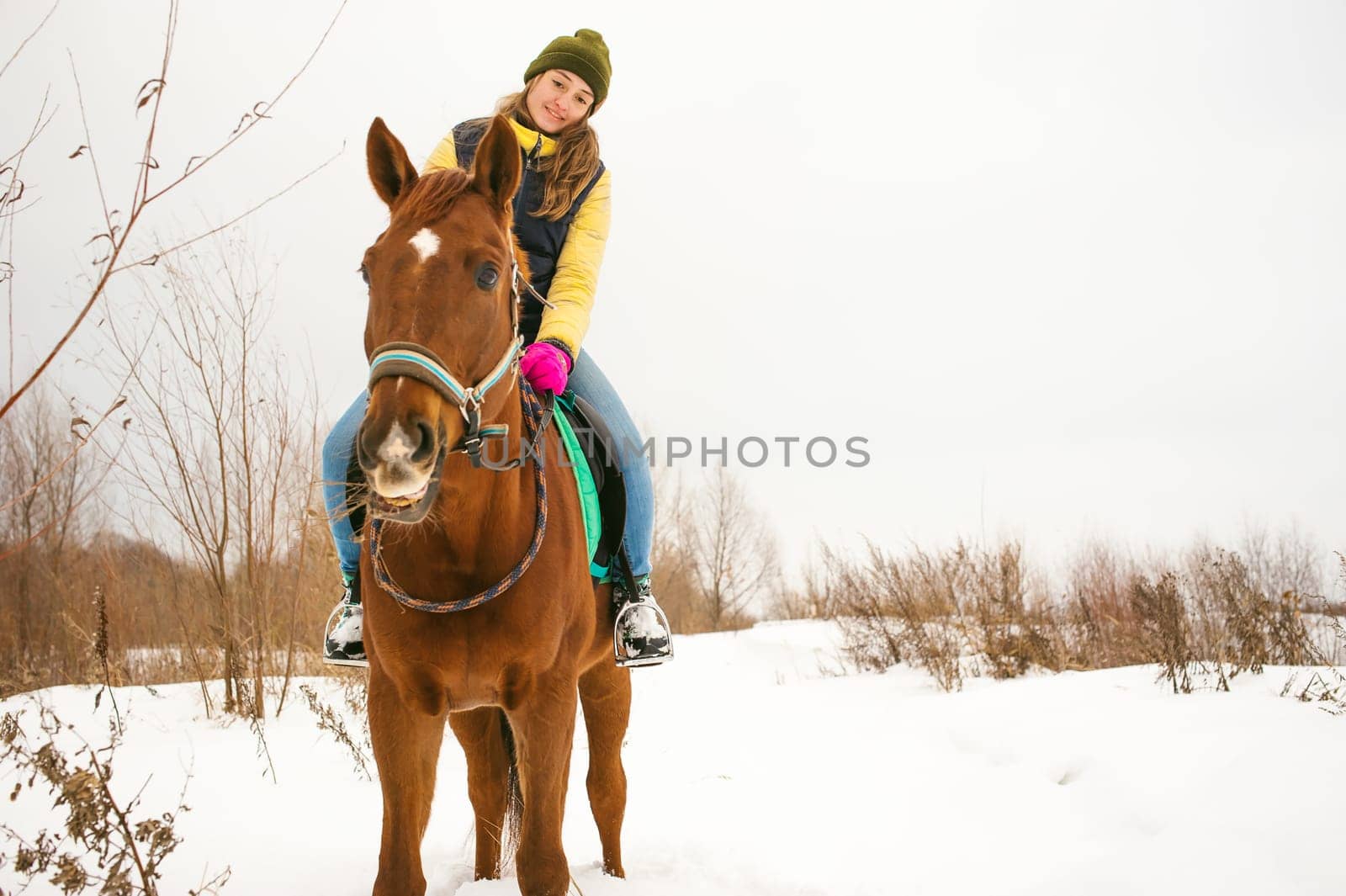 Woman in winter clothes is riding on a horse on a background of white snow.