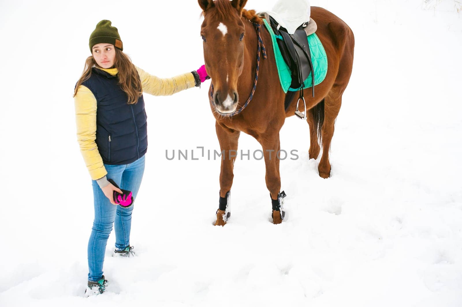 Woman in winter clothes and the horse stand together against the white snow. love and care for horses. animal portrait on a white background.