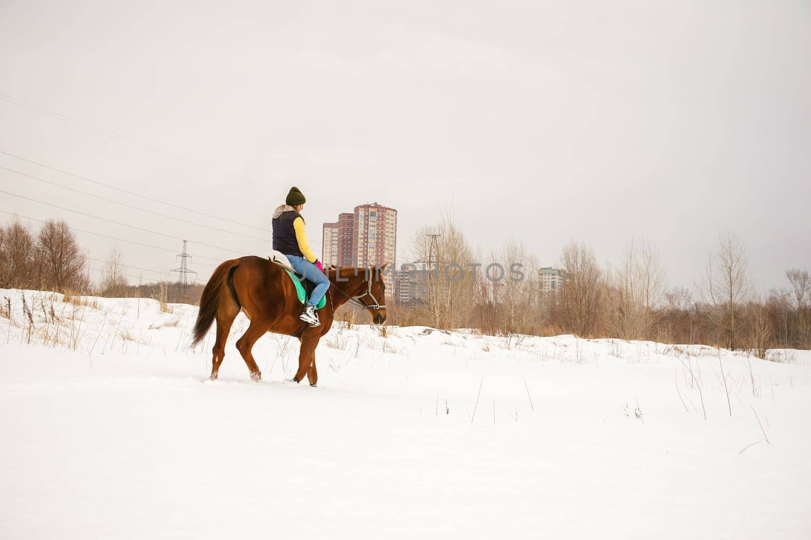 Woman in winter clothes is riding on a horse on a background of white snow.