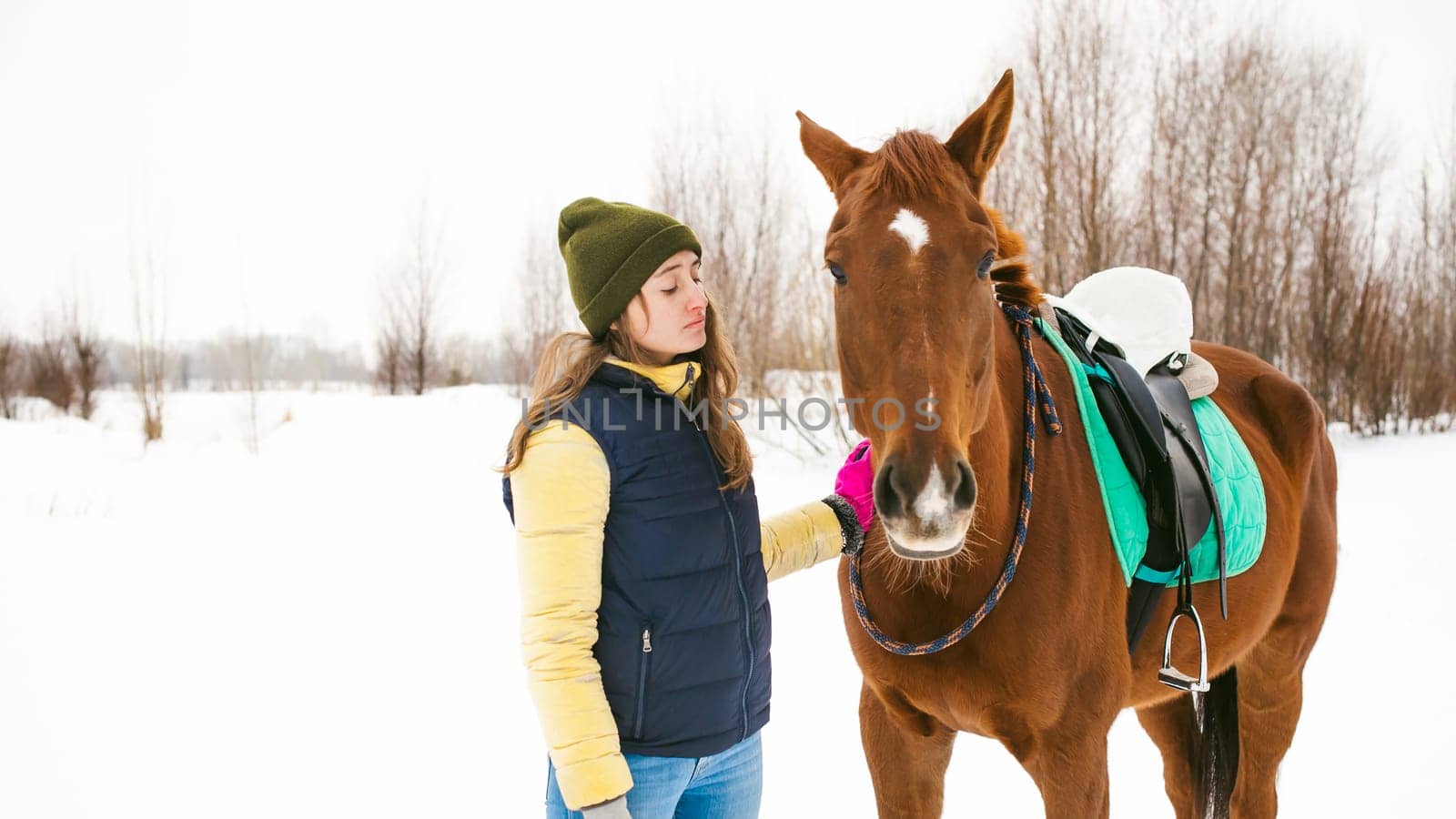Woman in winter clothes and the horse stand together against the white snow. love and care for horses. animal portrait on a white background.