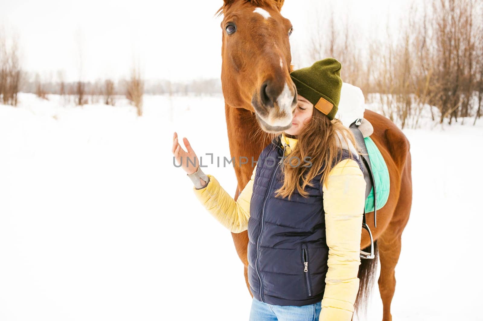 Female rider and horse in the open air. portrait of a beautiful young woman with her stallion, outdoors in winter. girl hugging and caressing the animal