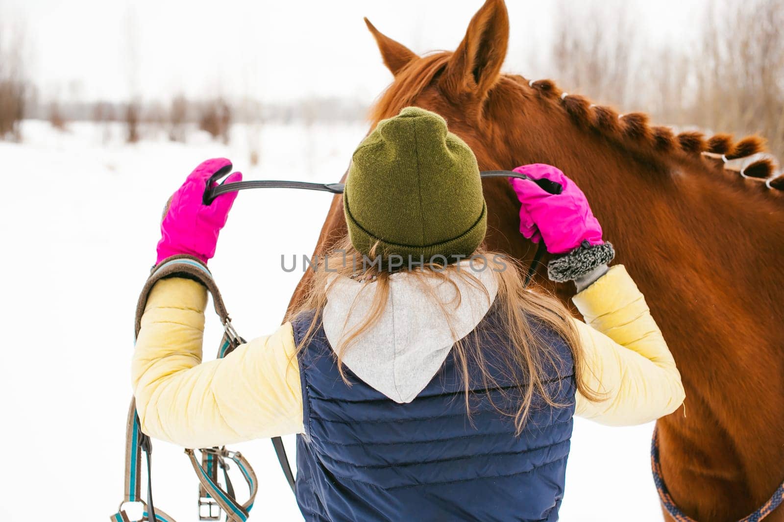Woman in winter clothes and the horse to stand together against the white snow. love and care for horses. girl puts a bridle on a horse