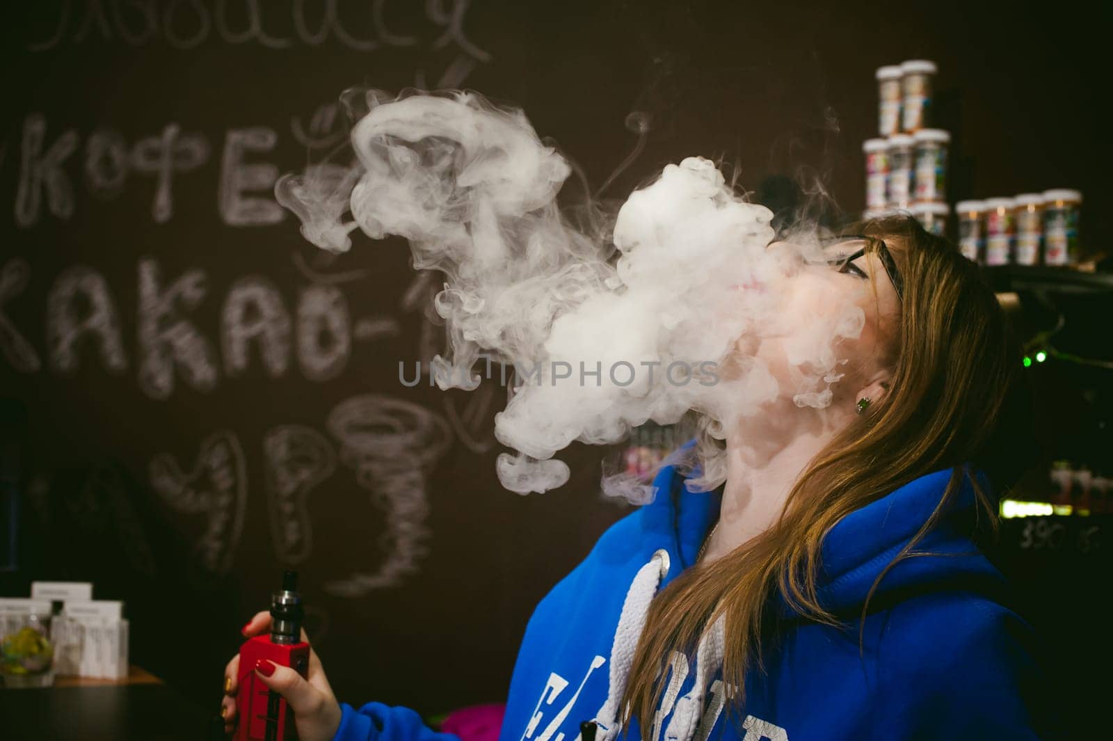 young Cute woman, the seller in vape shop shop, smoking electronic cigarette,  vaping and releases a cloud of vapor