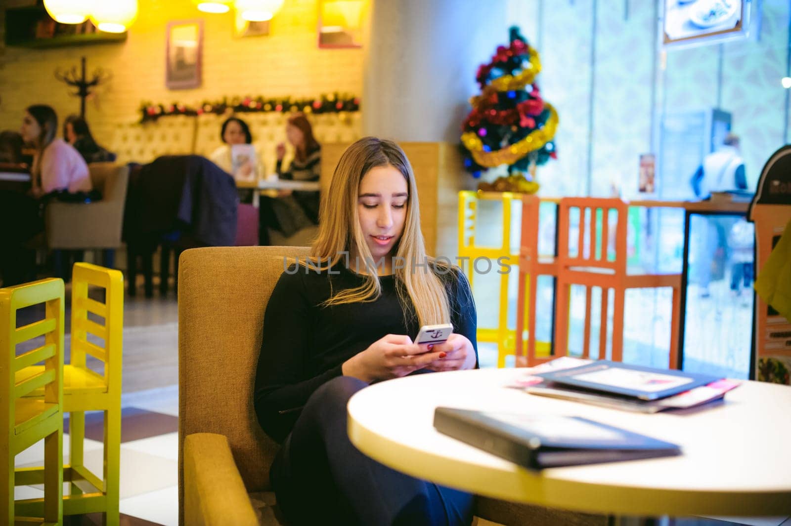 woman in a cafe. young girl sitting at a table in a black dress and looking into the smartphone