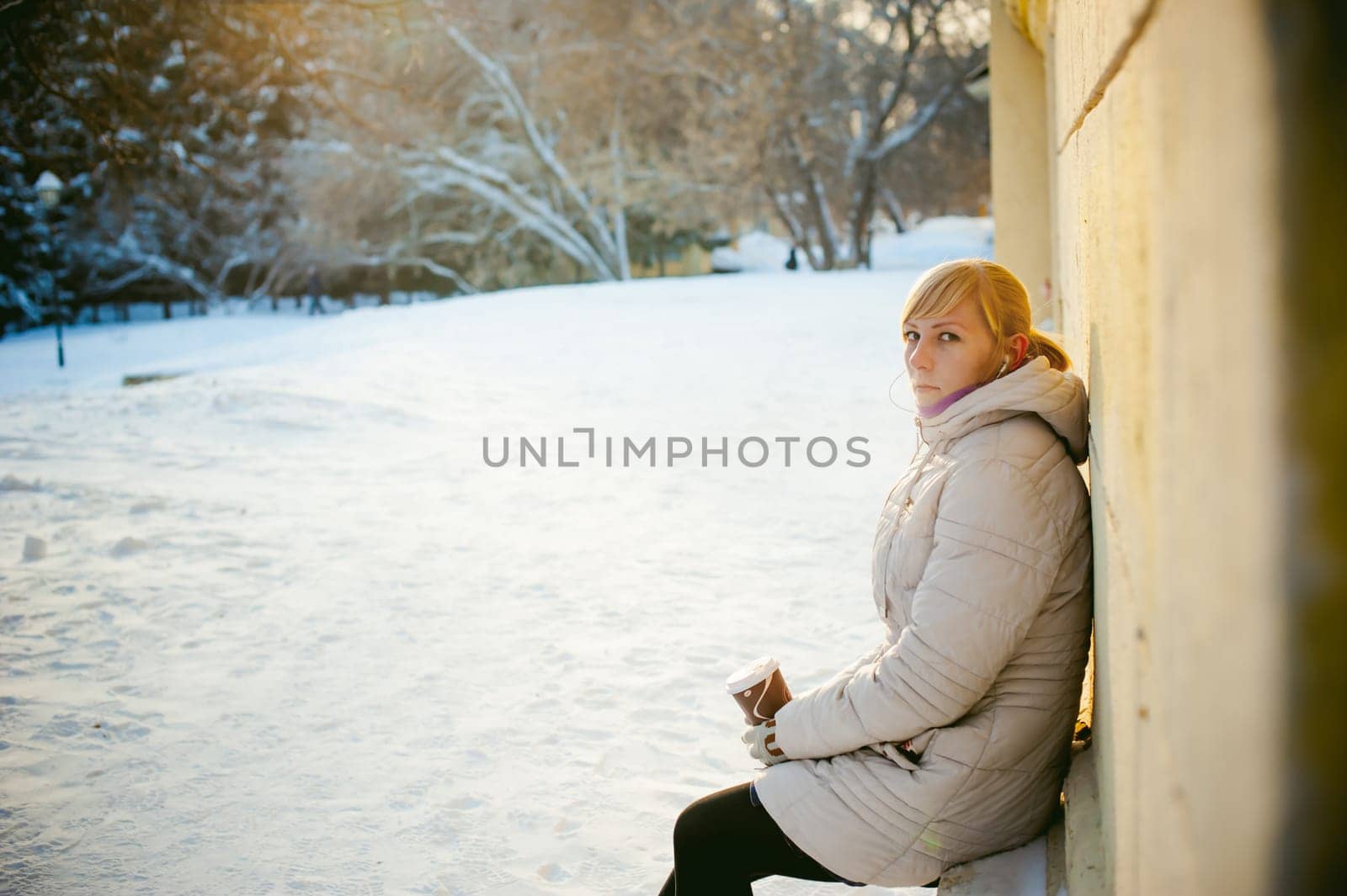 young woman dressed in warm clothes drinking takeaway coffee from the cup on the street in winter