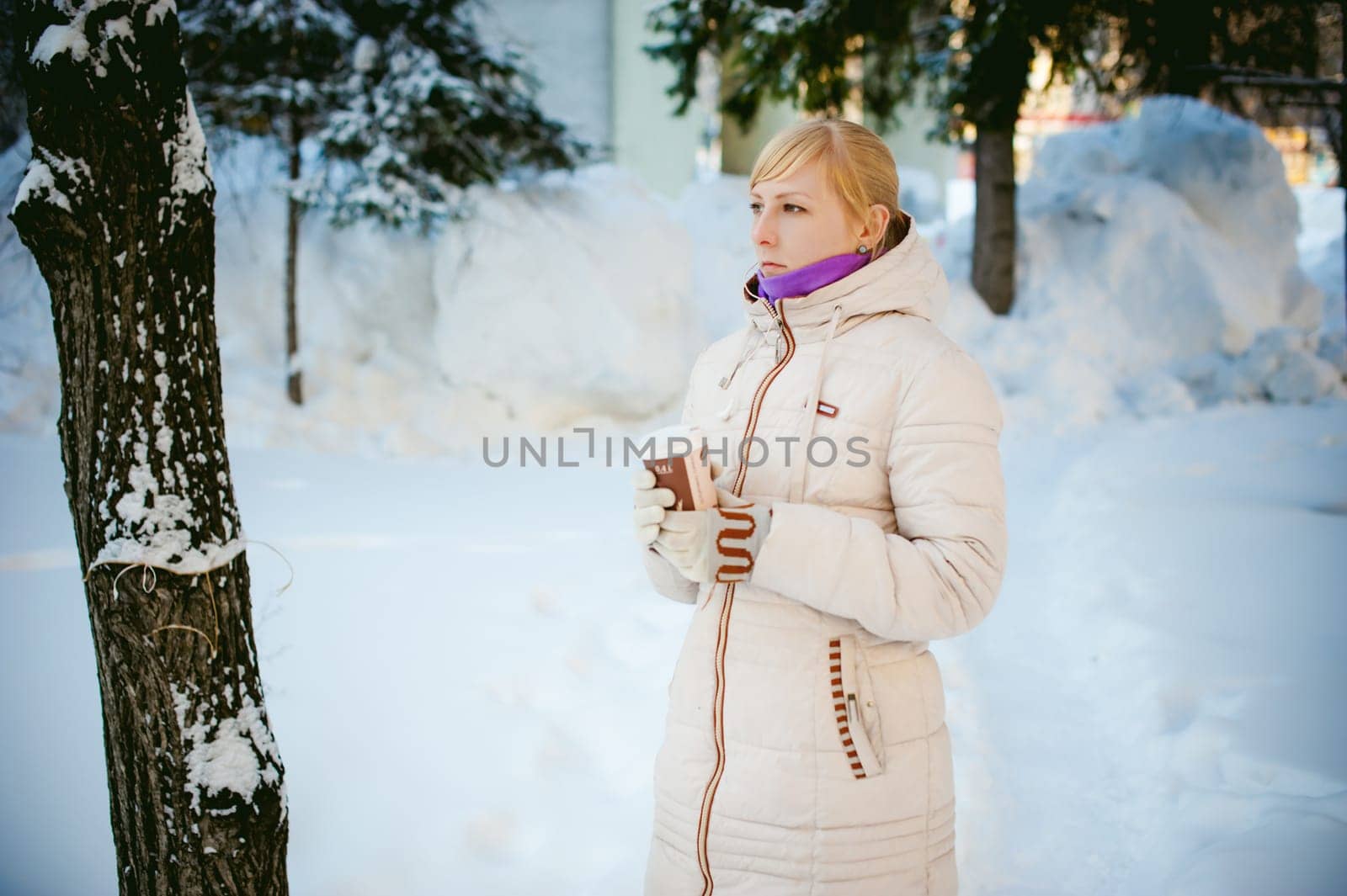 young woman dressed in warm clothes drinking takeaway coffee from the cup on the street in winter