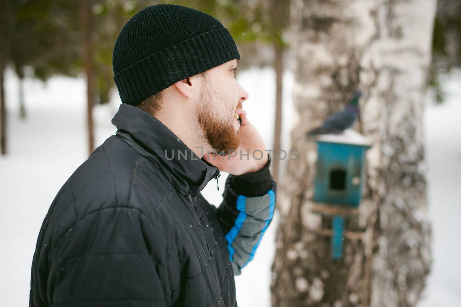 a young man with a beard, smokes an electronic cigarette and happily talking on the phone through the Internet, a positive relaxing outdoors in the snow in the winter
