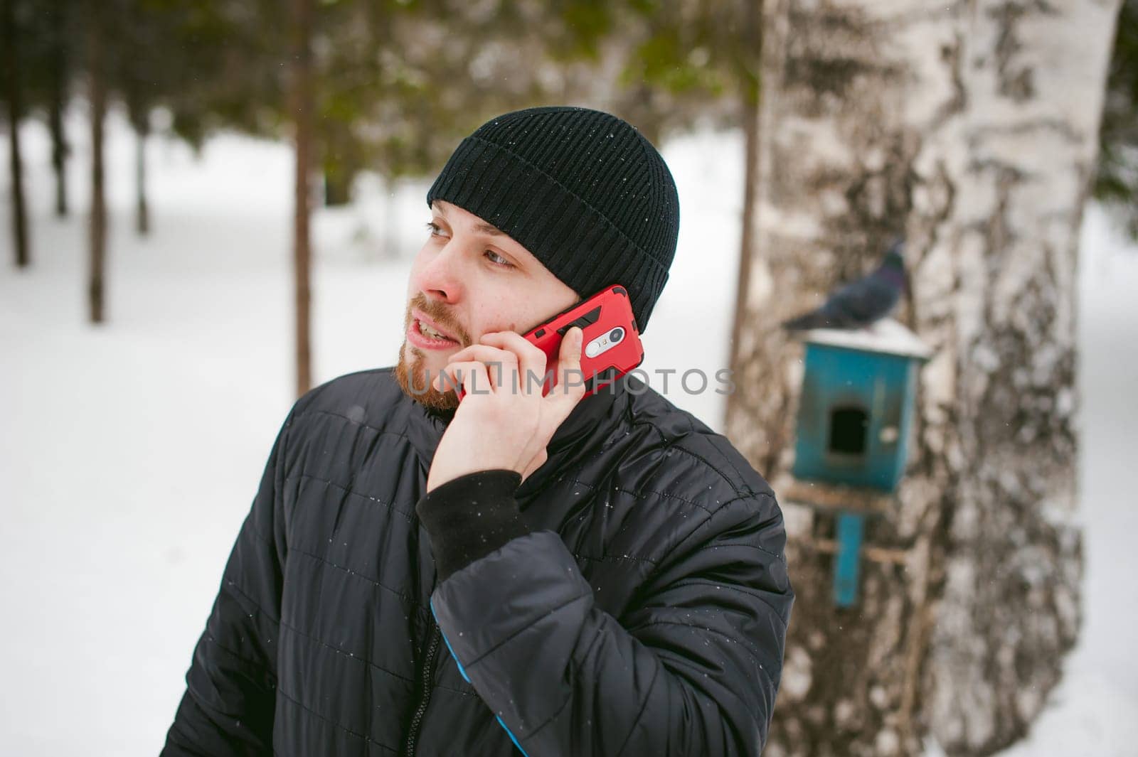 a young man with a beard, smokes an electronic cigarette and happily talking on the phone through the Internet, a positive relaxing outdoors in the snow in the winter