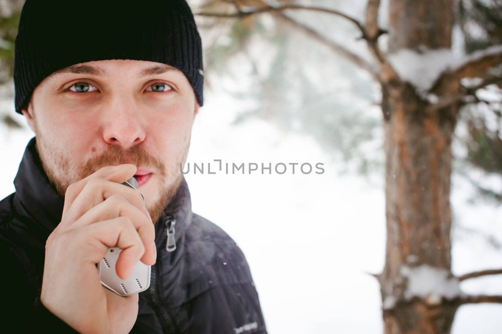 a young man with a beard, smokes an electronic cigarette, outdoors in winter snow