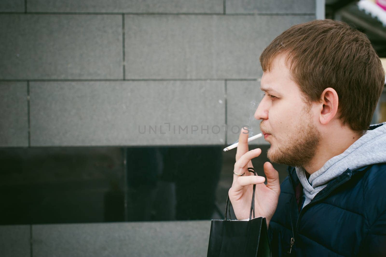 Portrait of a man with a beard with a mustache, smoking a cigarette, with an emotional face in the open air