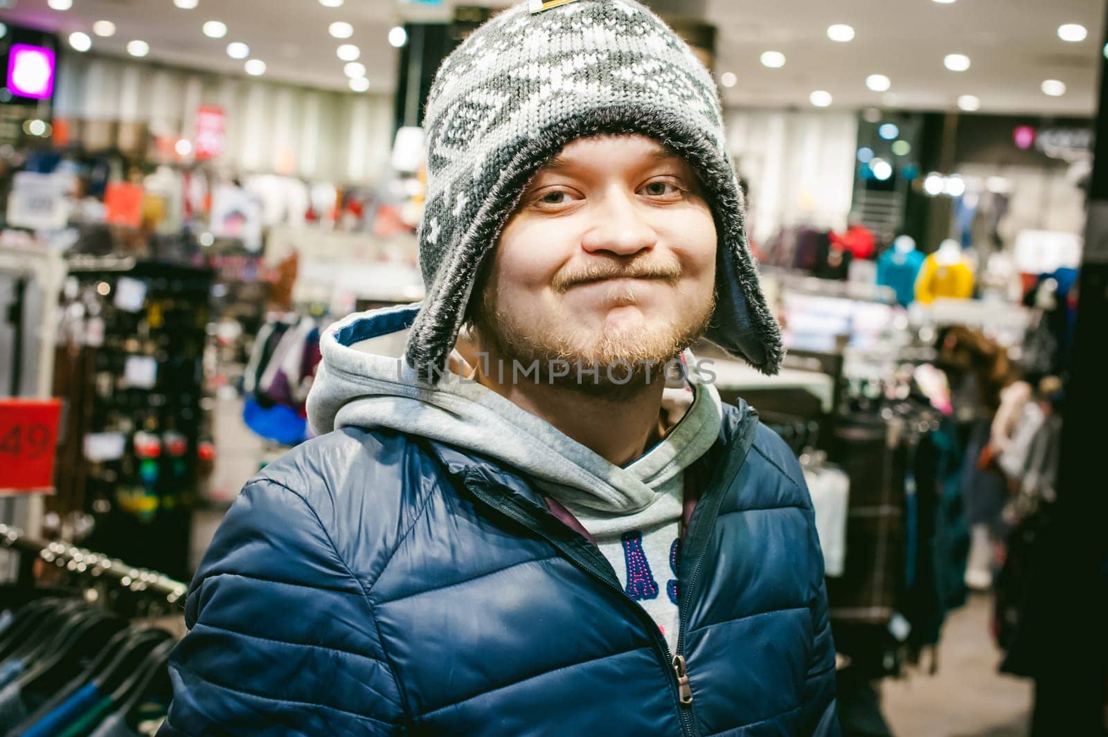 Portrait of a man with a beard with a mustache, putting on winter spring knitted hats in the store, with an emotional face shopping