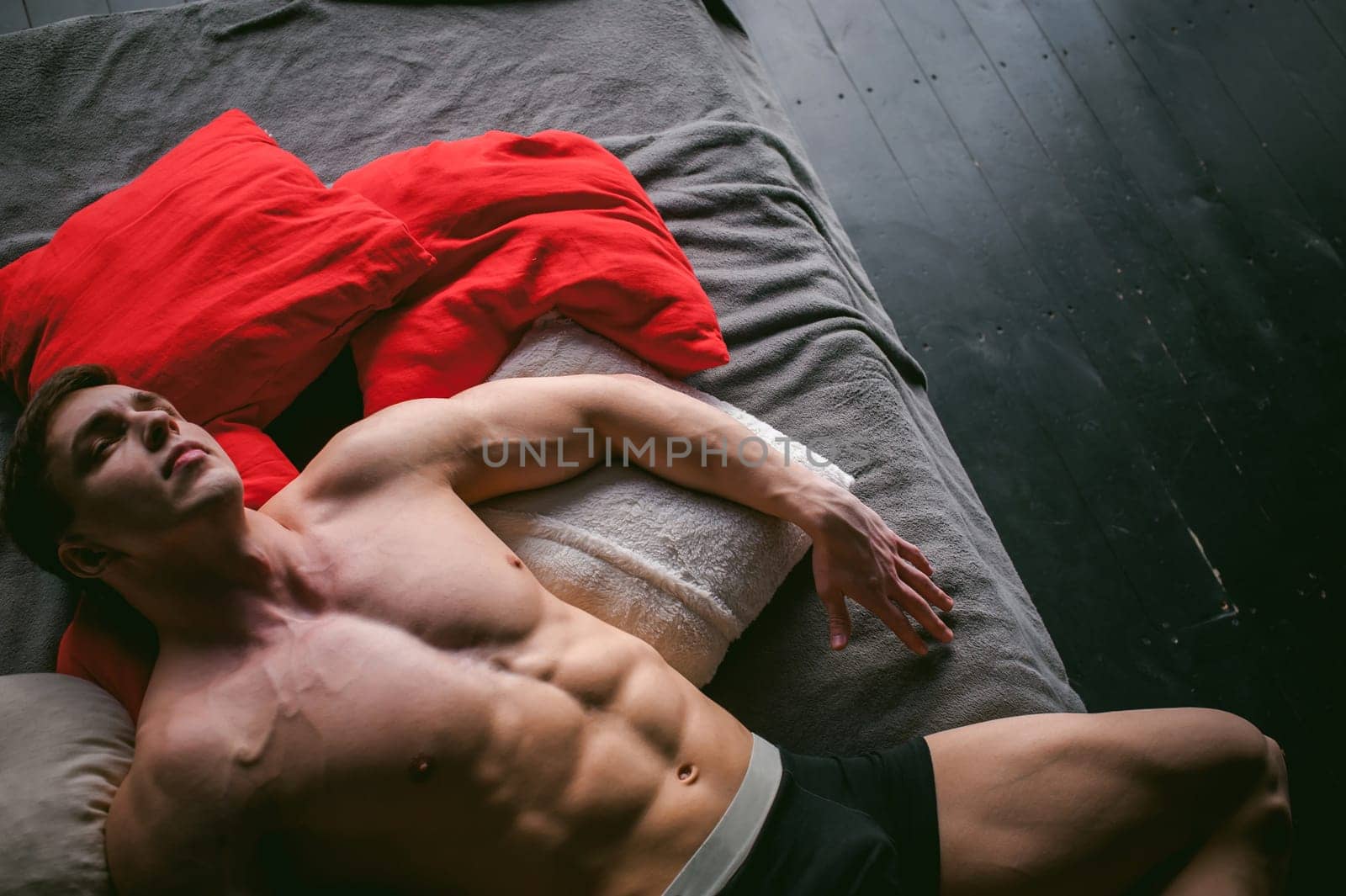studio portrait young sexy men bodybuilder athlete, with a bare torso, lies on a bed in pillows in underwear