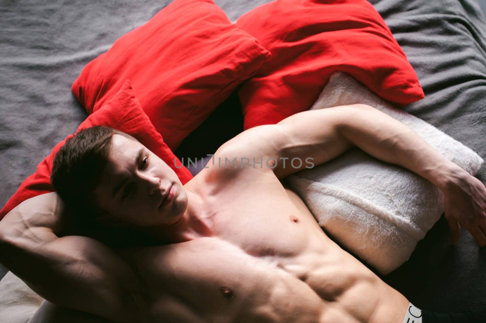 studio portrait young sexy men bodybuilder athlete, with a bare torso, lies on a bed in pillows in underwear