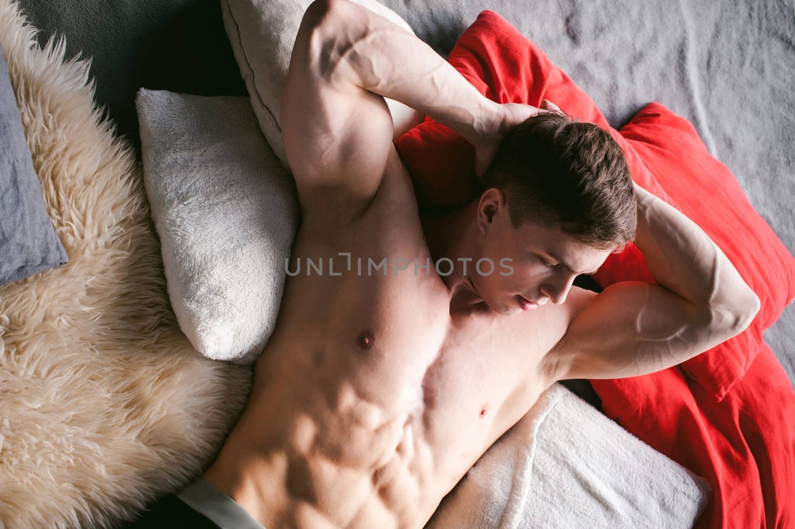 studio portrait young sexy men bodybuilder athlete, with a bare torso, lies on a bed in pillows in underwear