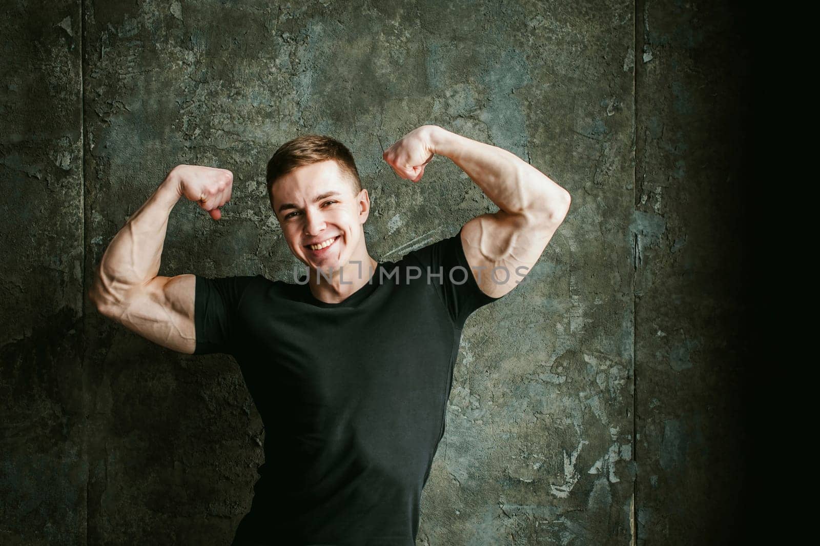 Young sexy men bodybuilder athlete, studio portrait loft on background of stylized Concrete brutal wall, guy model black Tshirt and trousers With powerful muscular arms demonstrates strength