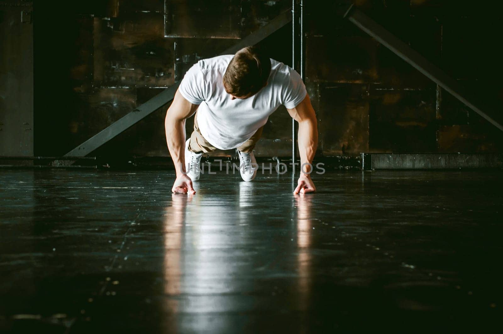 Young sexy male bodybuilder athlete with a bare torso. portrait of a studio of a light-skinned strong man engaged in push-ups on the fists, on the floor, straining powerful hands