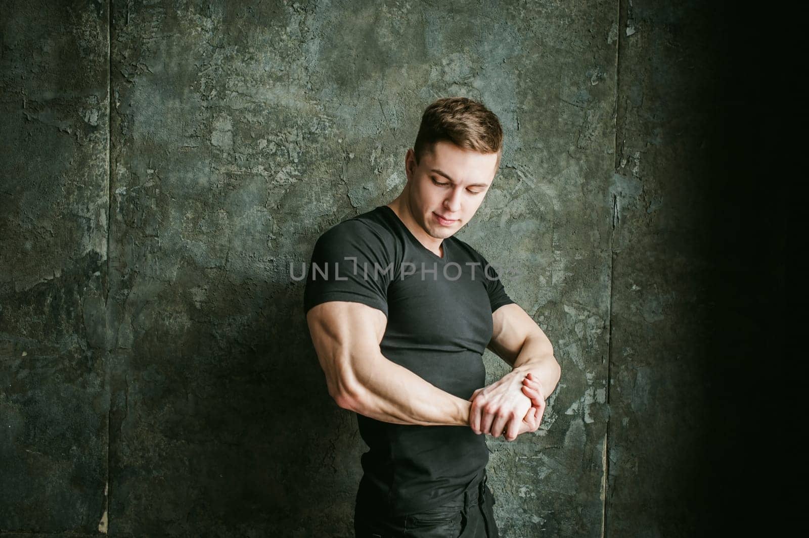 Young sexy men bodybuilder athlete, studio portrait loft on background of stylized Concrete brutal wall, guy model black Tshirt and trousers With powerful muscular arms demonstrates strength