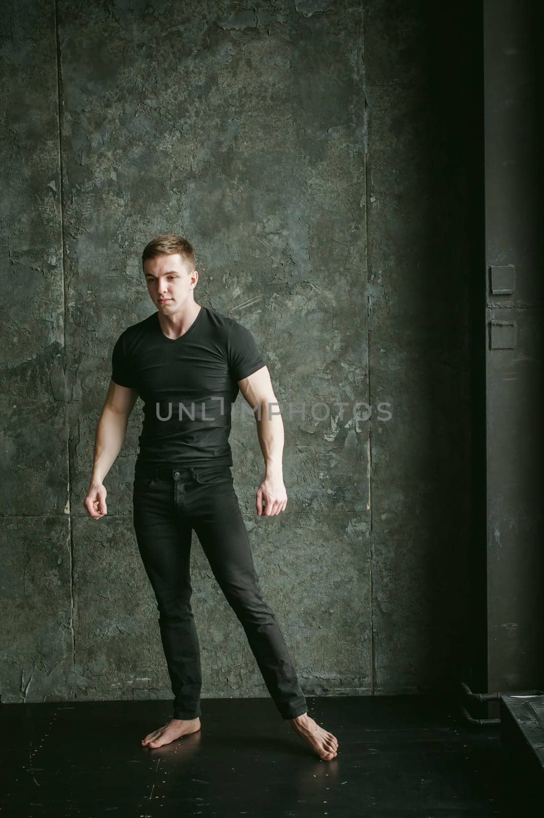 Young sexy men bodybuilder athlete, studio portrait loft on background of stylized Concrete brutal wall, guy model black Tshirt and trousers