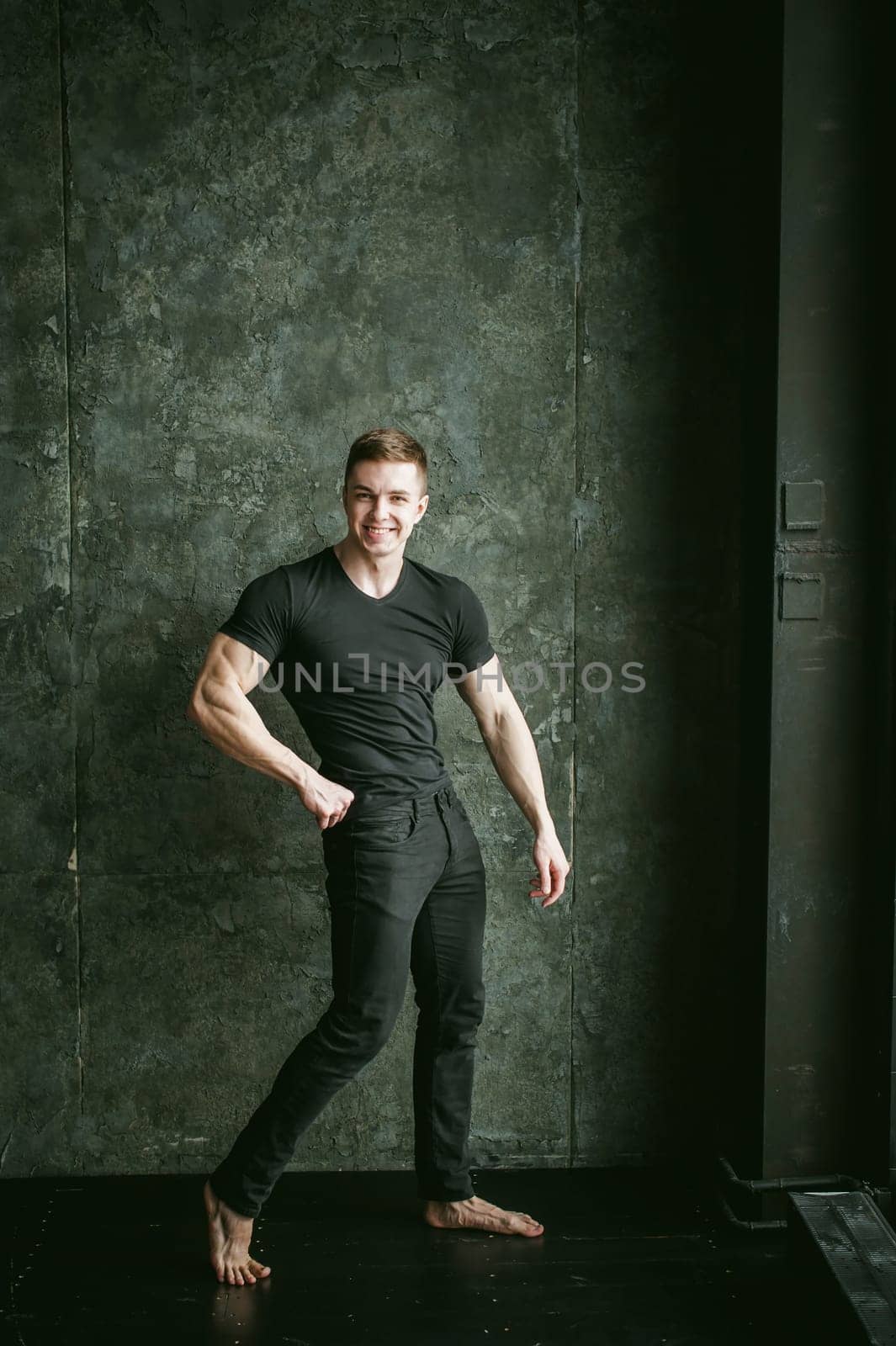 Young sexy men bodybuilder athlete, studio portrait loft on background of stylized Concrete brutal wall, guy model black Tshirt and trousers