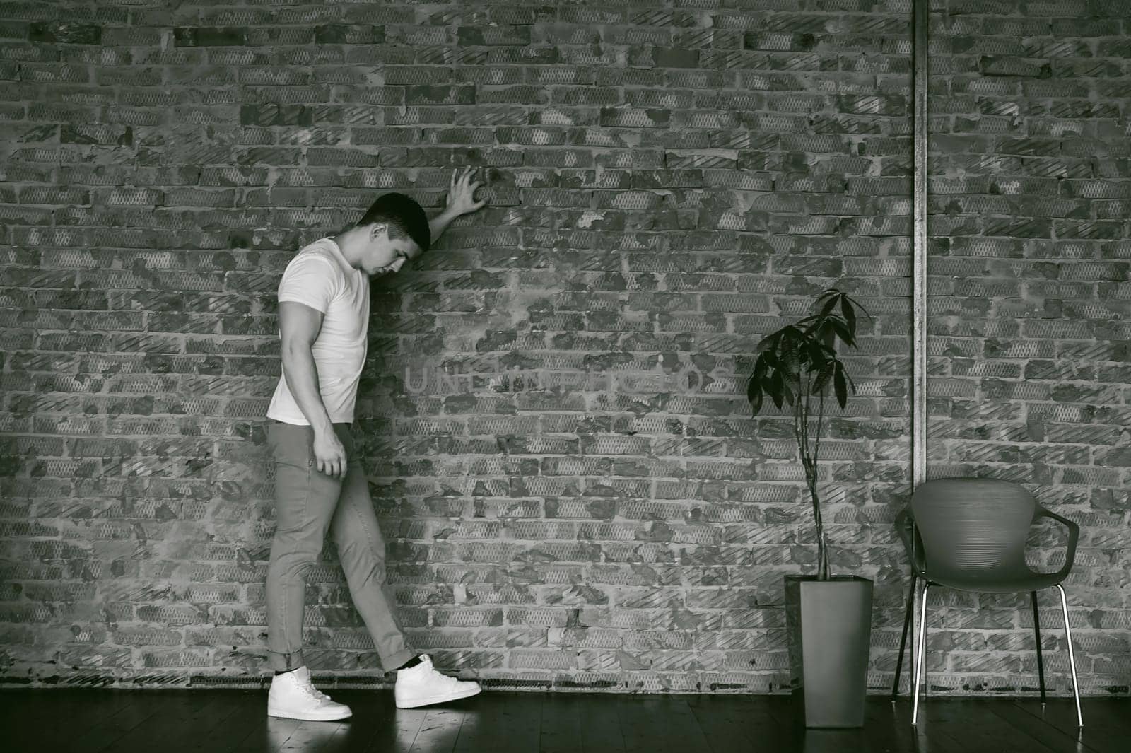 Young sexy men bodybuilder athlete,studio portrait in loft, guy model in white T-shirt and brown trousers, Leaned against a brick wall