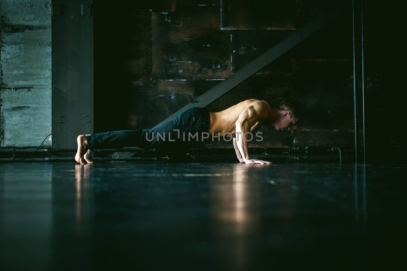Young sexy male bodybuilder athlete with a bare torso. portrait of a studio of a light-skinned strong man engaged in push-ups, on the floor, straining powerful hands
