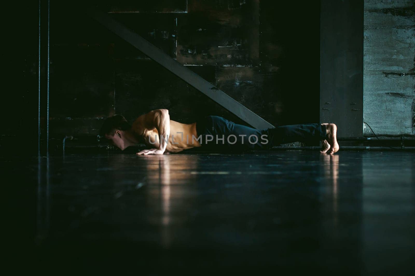 Young sexy male bodybuilder athlete with a bare torso. portrait of a studio of a light-skinned strong man engaged in push-ups, on the floor, straining powerful hands