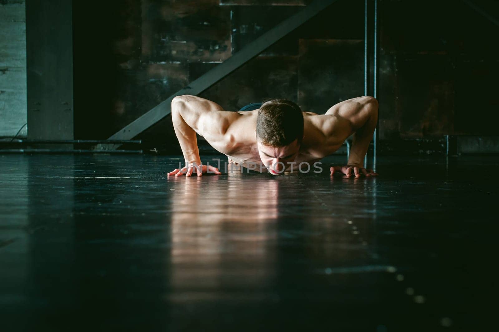 Young sexy male bodybuilder athlete with a bare torso. portrait of a studio of a light-skinned strong man engaged in push-ups, on the floor, straining powerful hands