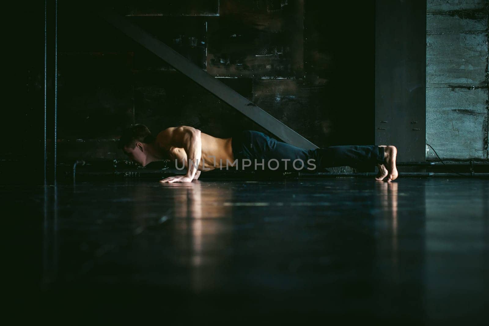 Young sexy male bodybuilder athlete with a bare torso. portrait of a studio of a light-skinned strong man engaged in push-ups, on the floor, straining powerful hands