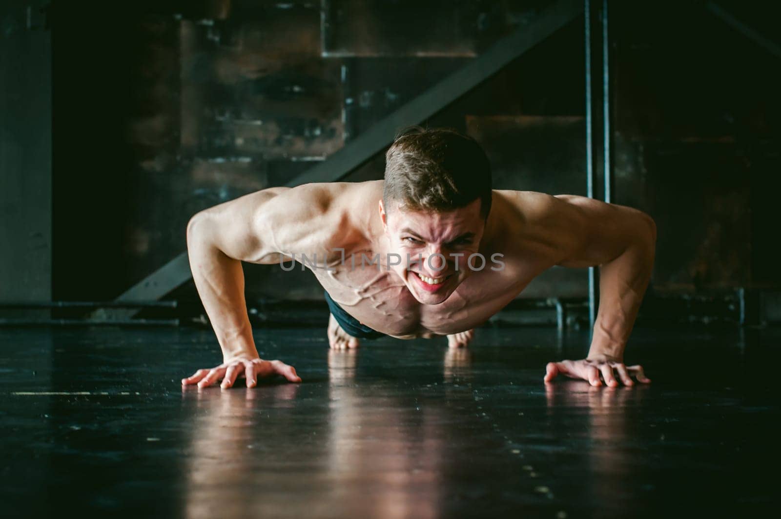 Young sexy male bodybuilder athlete with a bare torso. portrait of a studio of a light-skinned strong man engaged in push-ups, on the floor, straining powerful hands