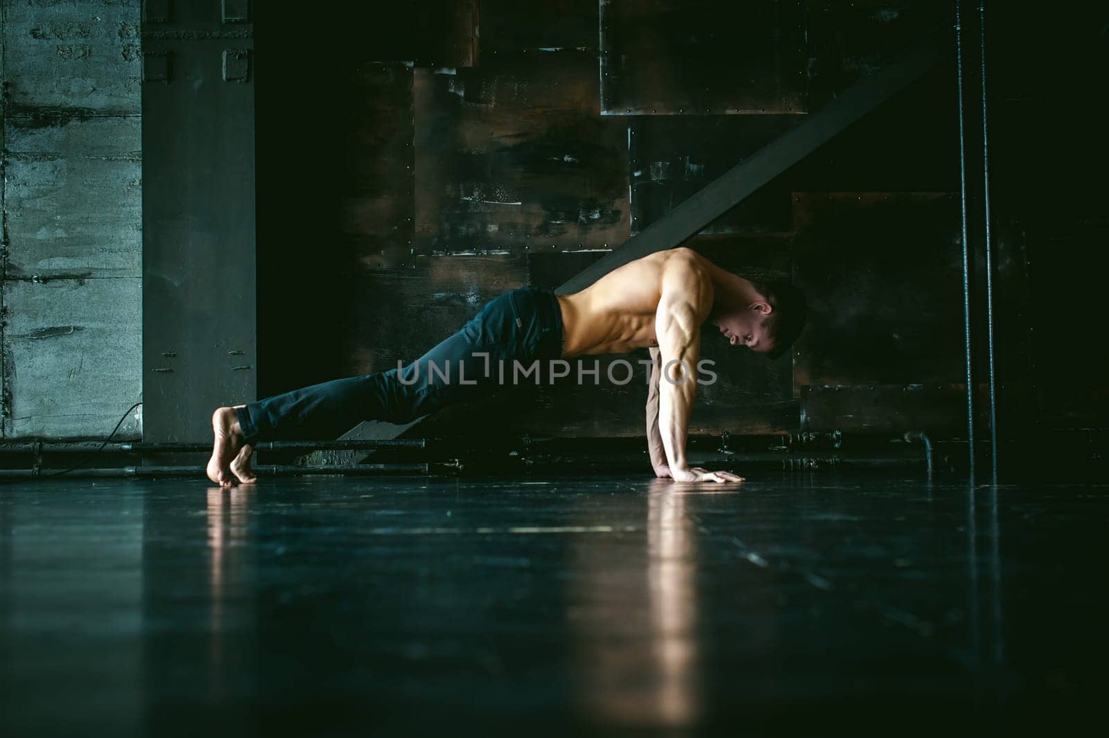 Young sexy male bodybuilder athlete with a bare torso. portrait of a studio of a light-skinned strong man engaged in push-ups, on the floor, straining powerful hands