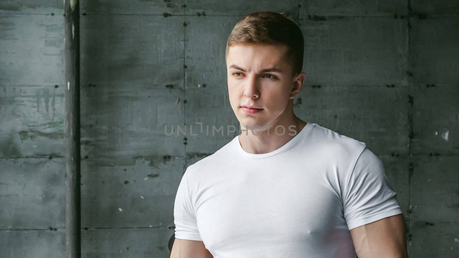 Young sexy men bodybuilder athlete,studio portrait in loft on the background of stylized wall and Black leather sofa, guy model in white T-shirt and brown trousers against background of larger window