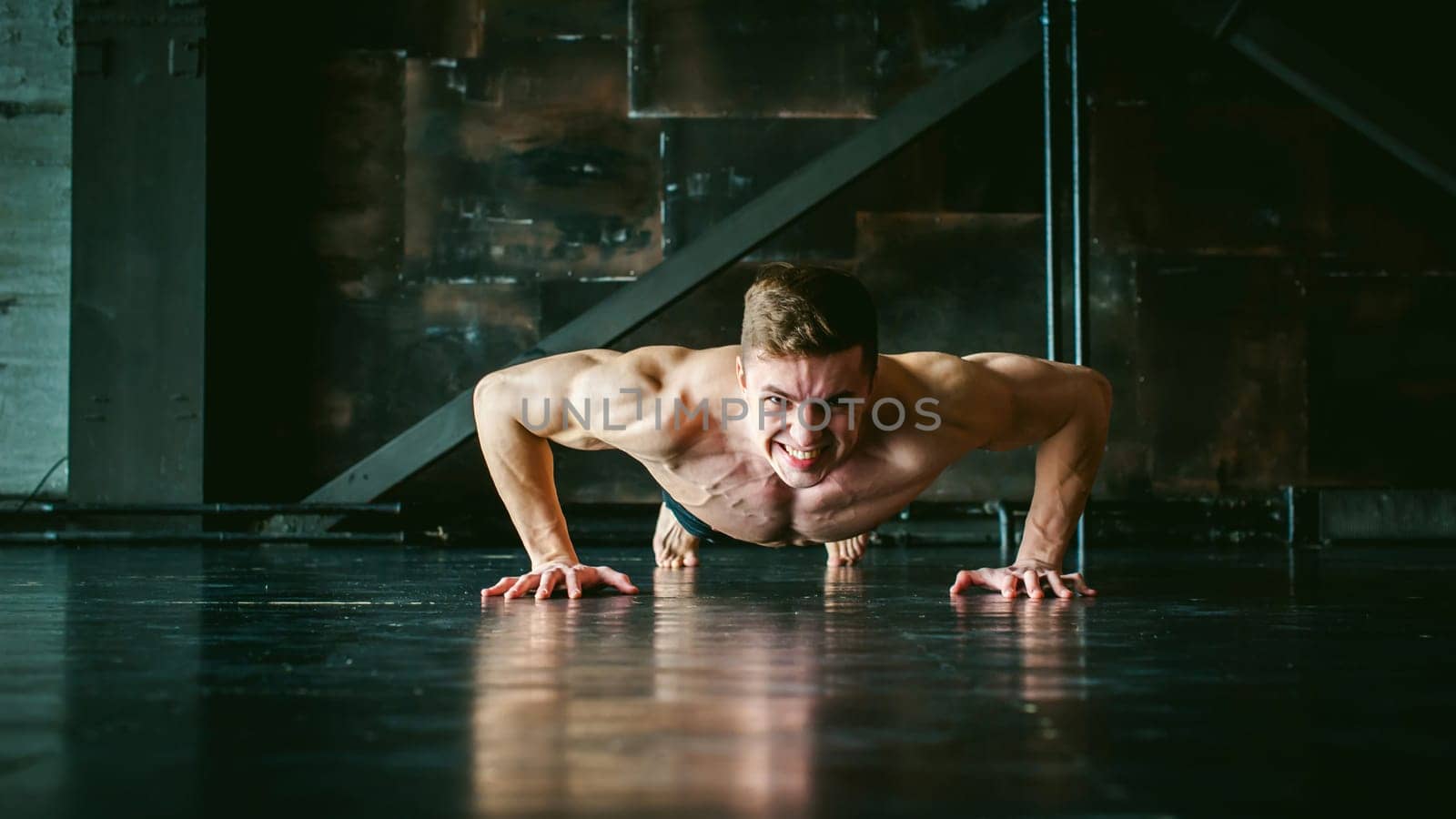 Young sexy male bodybuilder athlete with a bare torso. portrait of a studio of a light-skinned strong man engaged in push-ups, on the floor, straining powerful hands